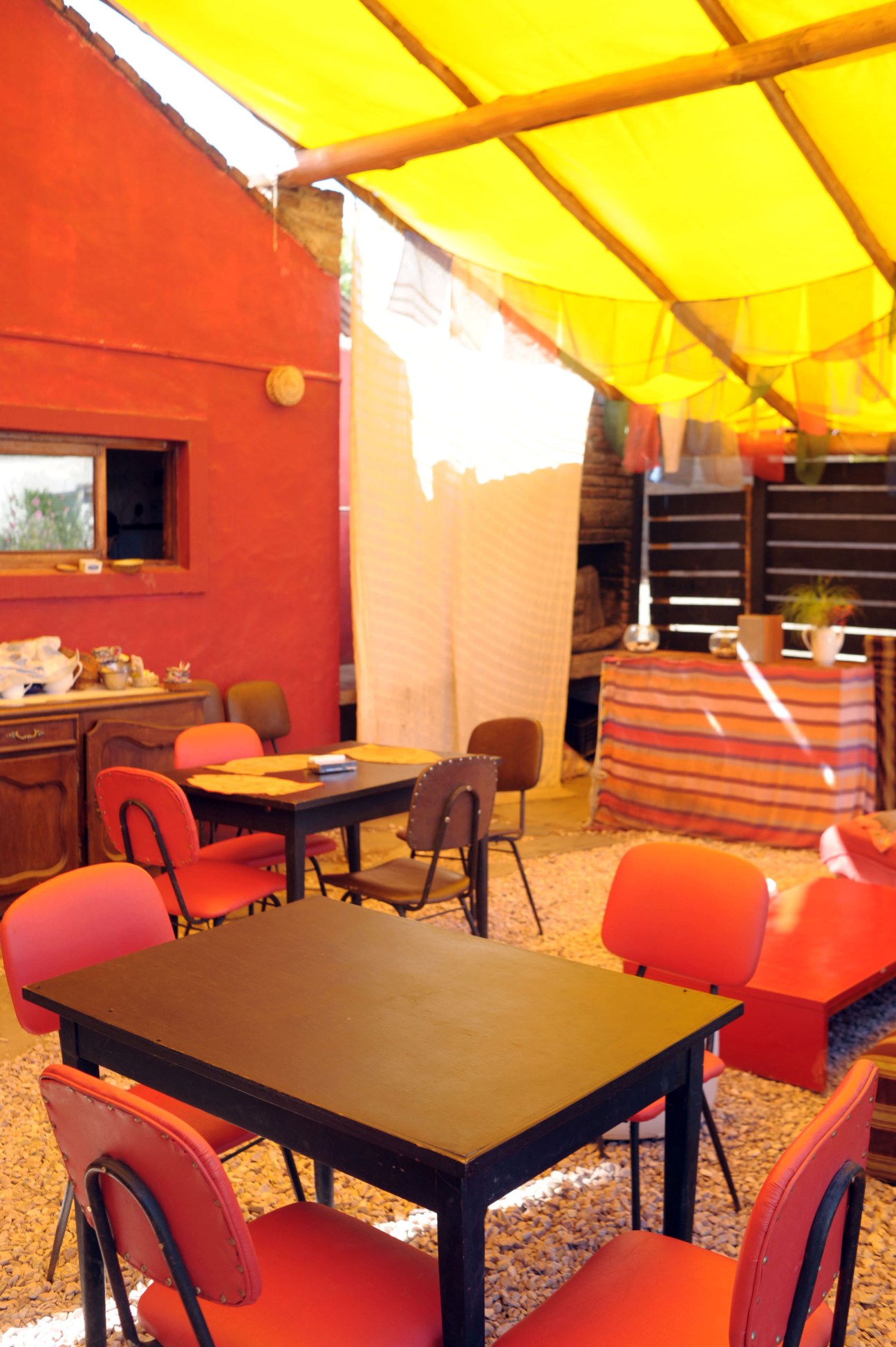 Interior of Casa Dulce tea spot with bright yellow canvas ceiling, red walls, and red chairs around black dining tables.