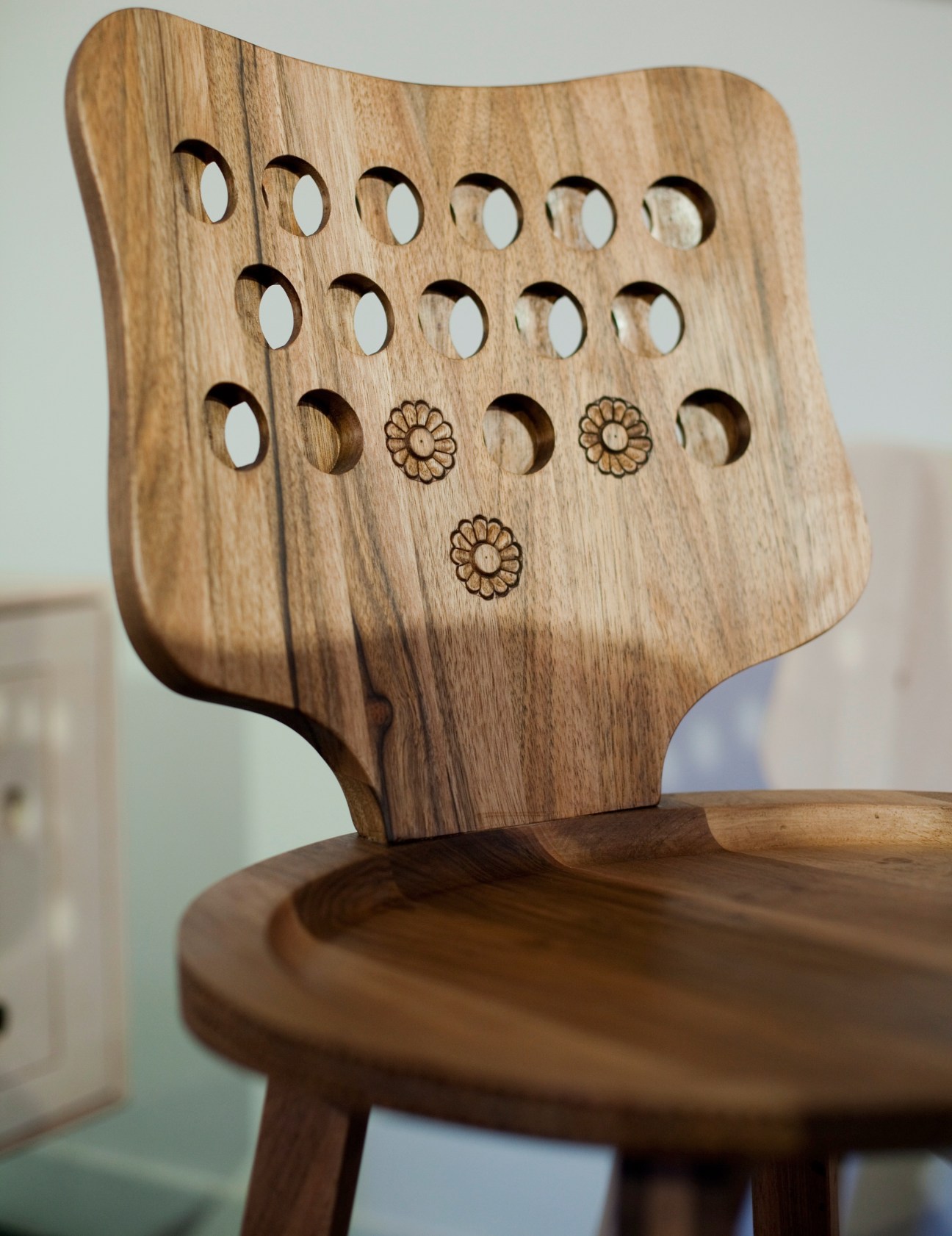 Wooden chair with carved oval holes and daisy flower motifs on backrest