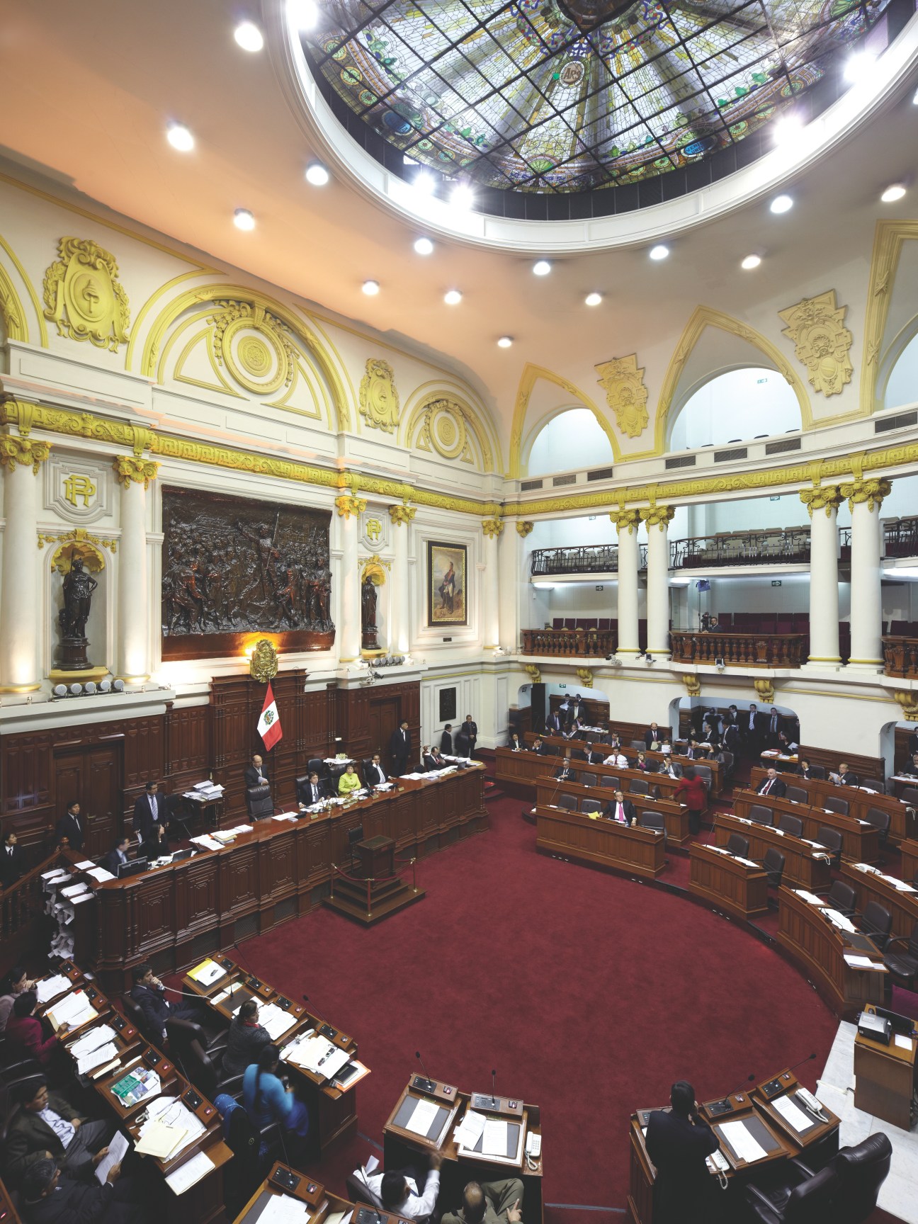 Interior of Peru's Congressional chamber with ornate gold decorative elements and seated legislators.