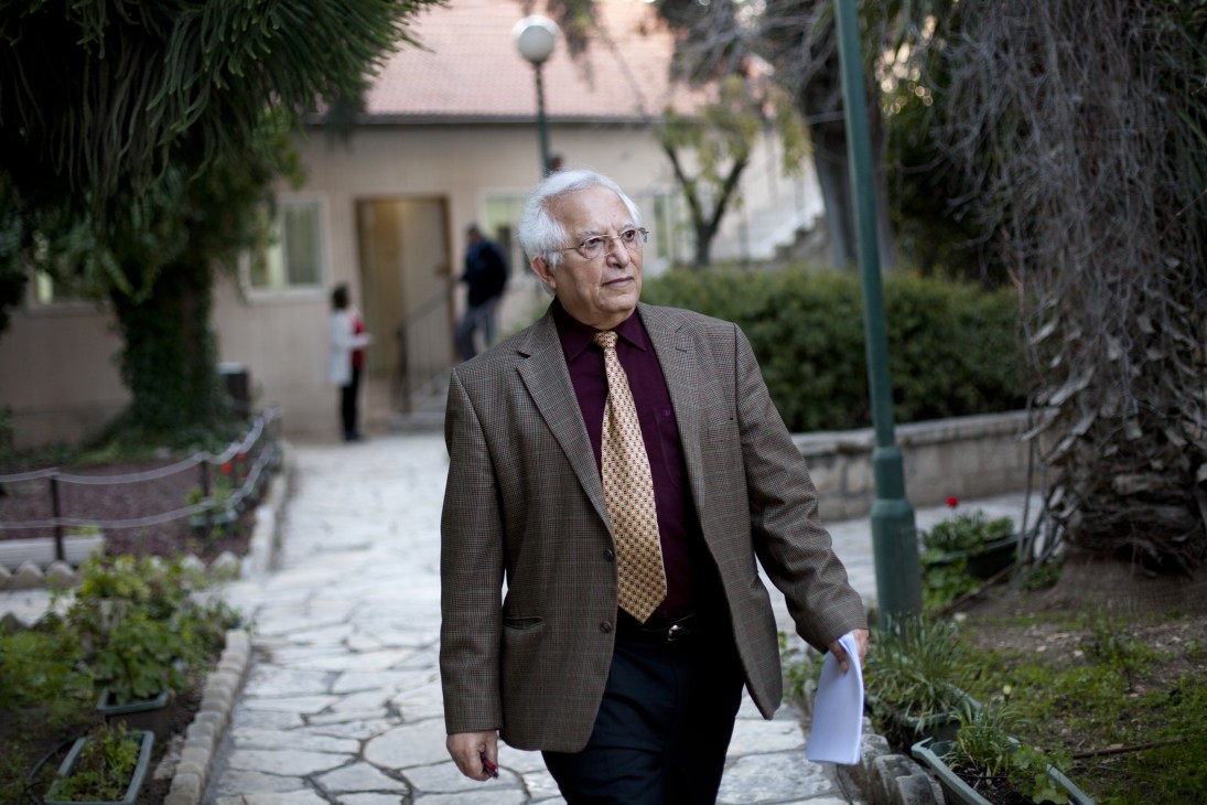 Menashe Amir walks through a courtyard in Jerusalem holding papers, heading to the radio studio.