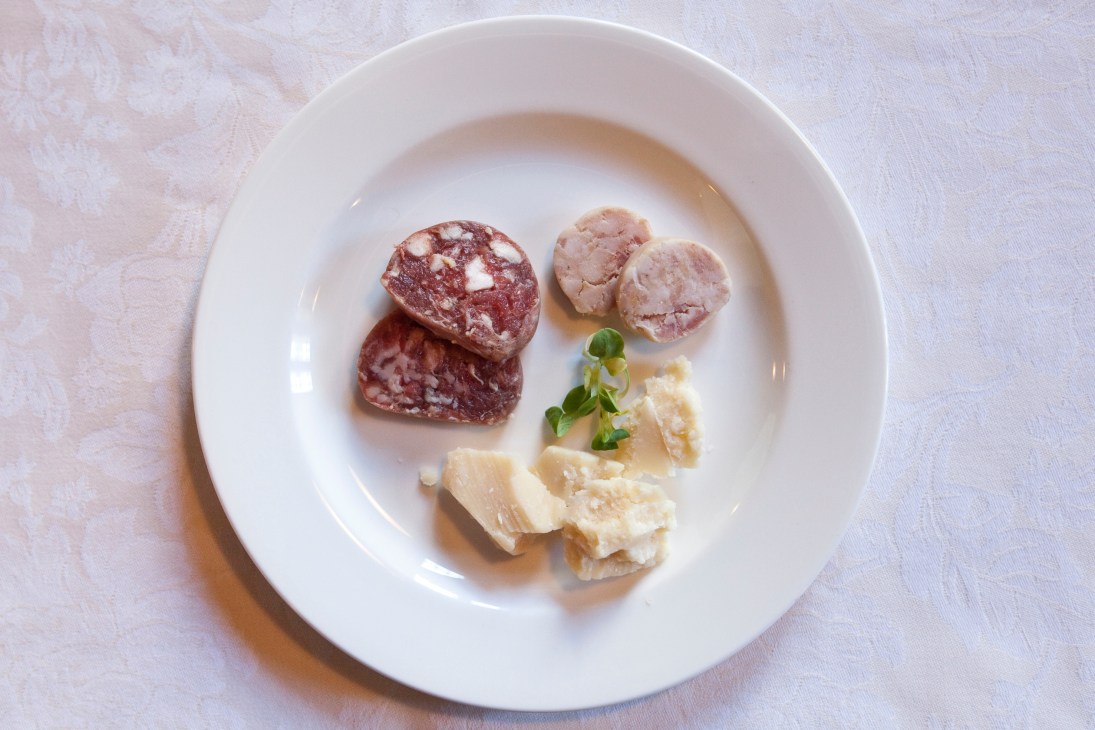 White plate with sliced salami, pale pâté rounds, and shaved cheese with parsley garnish.