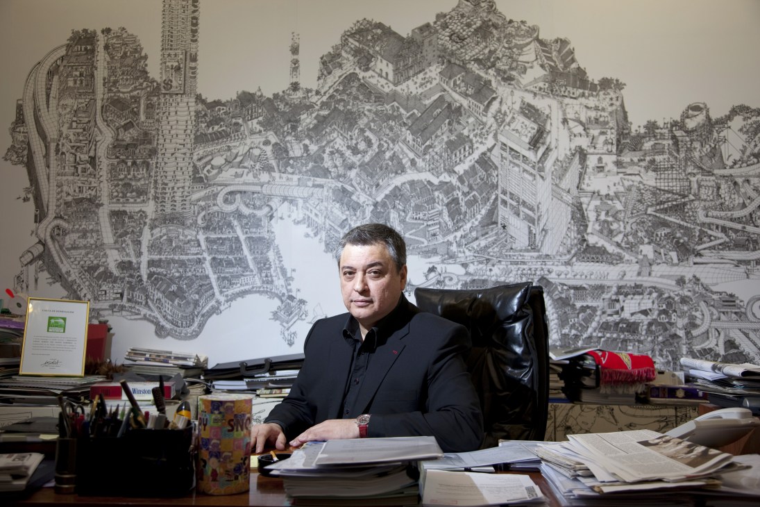 Architect Carlos Marreiros sits at his desk in front of a detailed architectural drawing of Macau's cityscape.