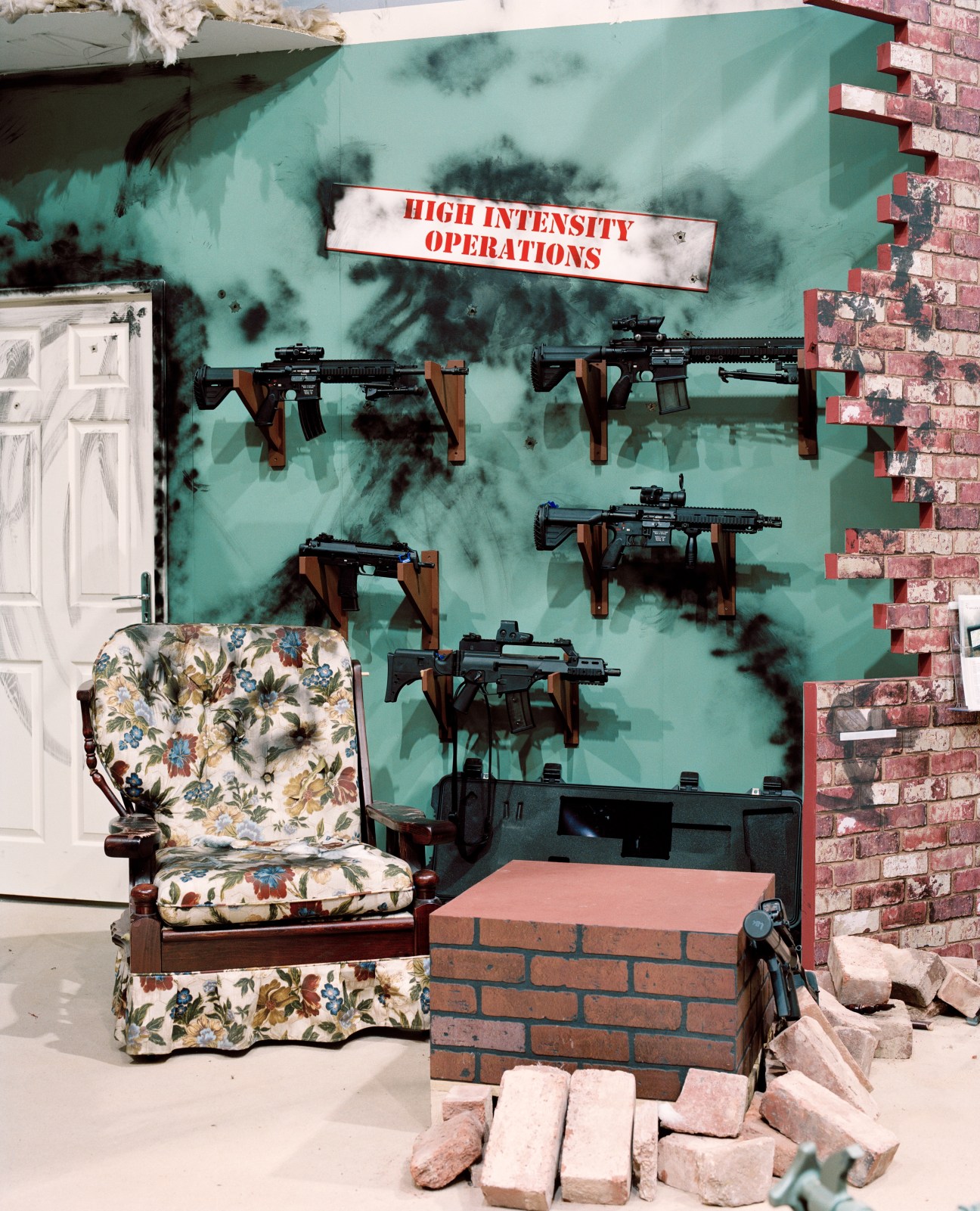 British Army small arms display with rifles mounted on turquoise wall behind floral armchair