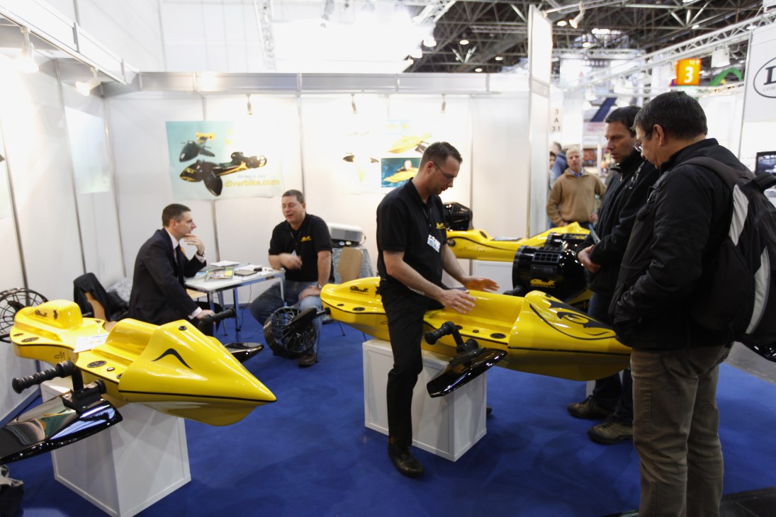 Yellow underwater scooters displayed at a trade show booth with visitors and staff.