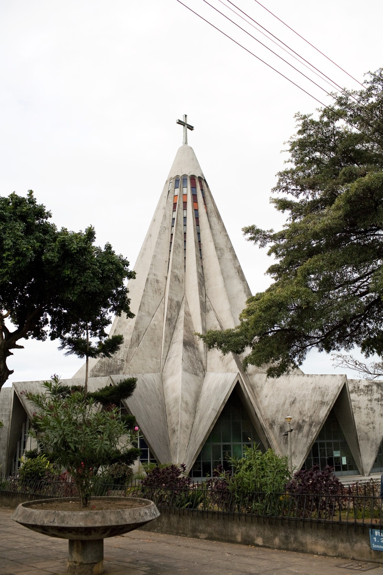 St Anthony's Church, a concrete modernist structure with a tall pointed spire topped by a cross, surrounded by trees.