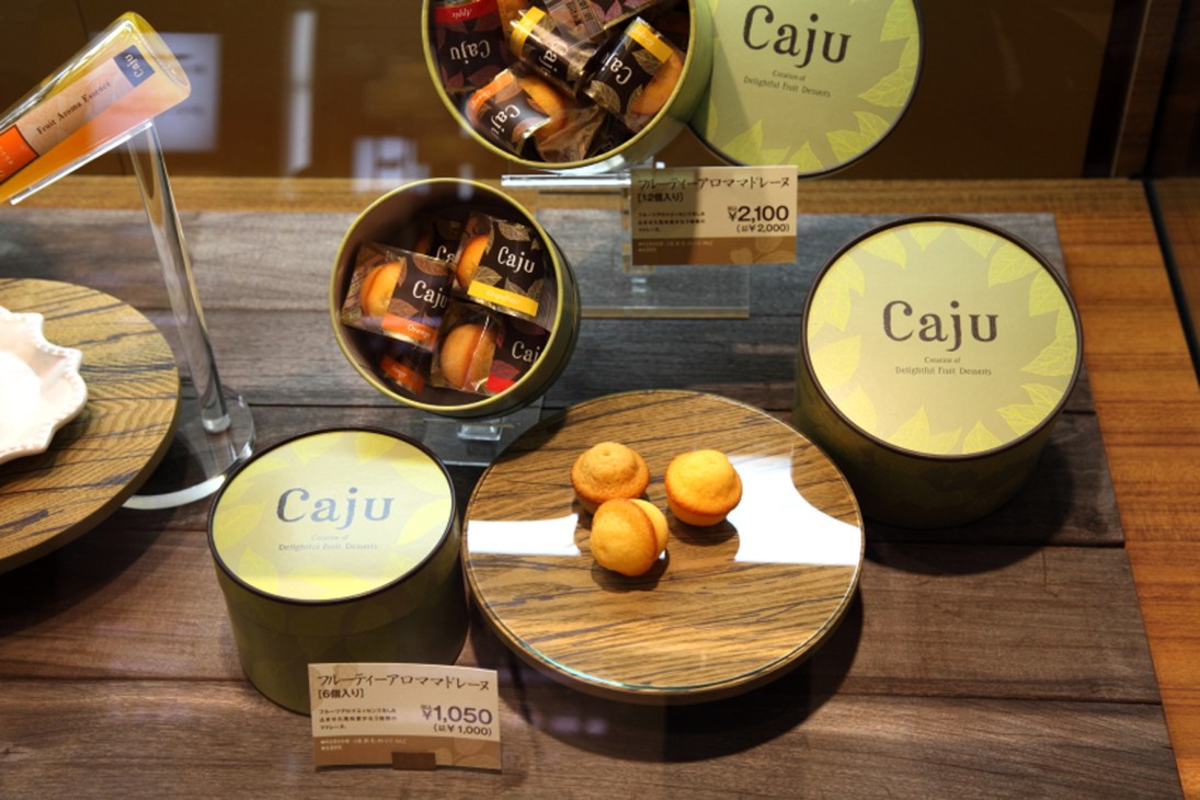 Caju fruit desserts displayed in yellow branded boxes and containers on a wooden surface at Mitsukoshi.