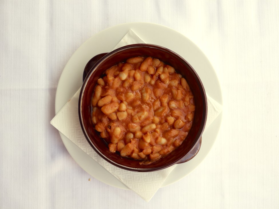 Stewed cannellini beans in tomato sauce served in a dark red bowl on a white plate.