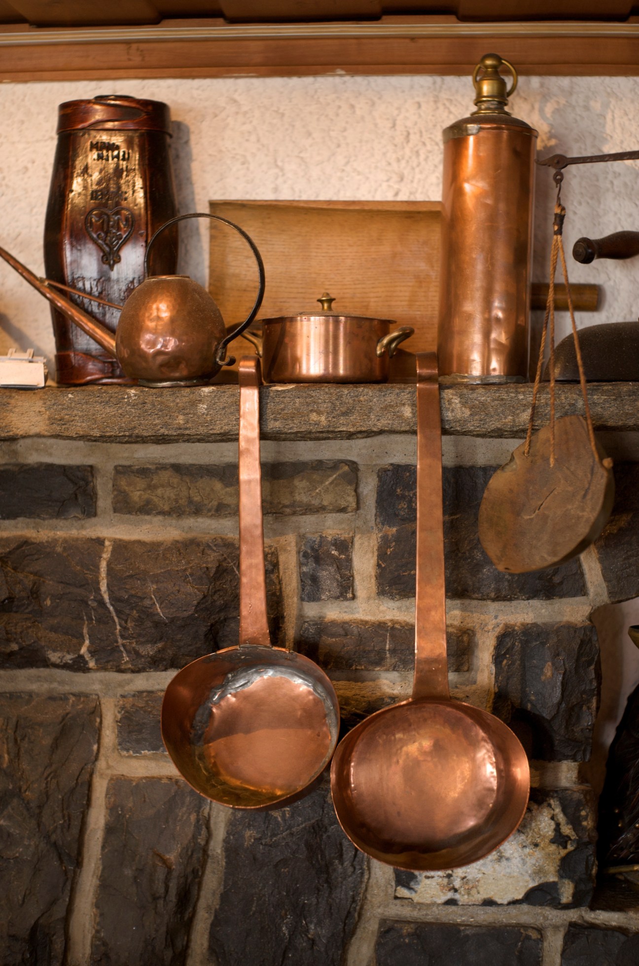 Vintage copper cooking utensils and kitchenware displayed on a stone fireplace mantel.