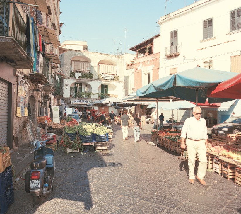 Antignano Market in Vomero with vendors, fresh produce, colorful umbrellas and Vespa parked on cobblestone street.