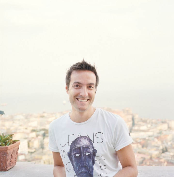 Luca Grossi, 32-year-old event organiser, smiling at camera with Naples cityscape behind him.