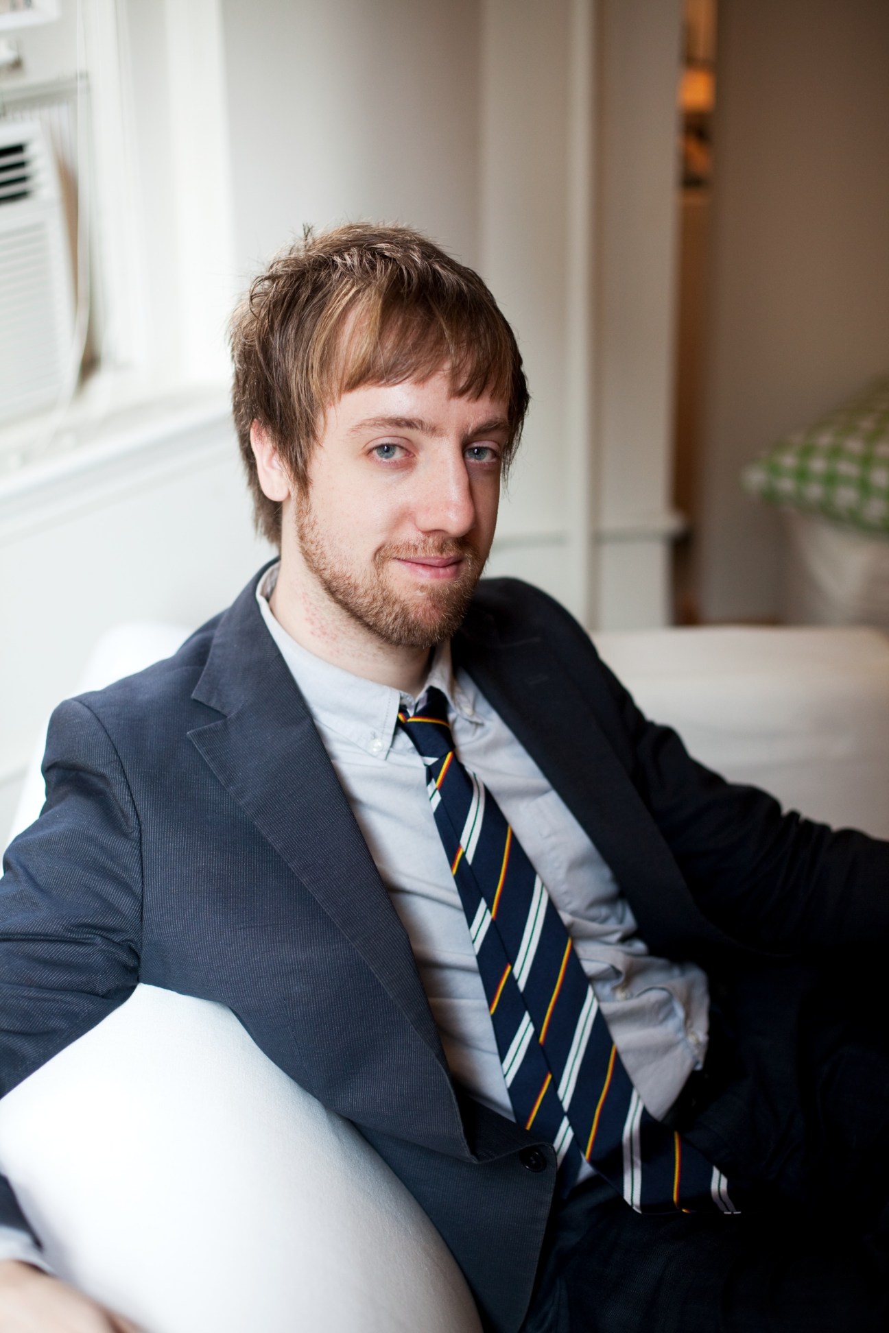 Man in navy blazer and striped tie seated in an office setting.