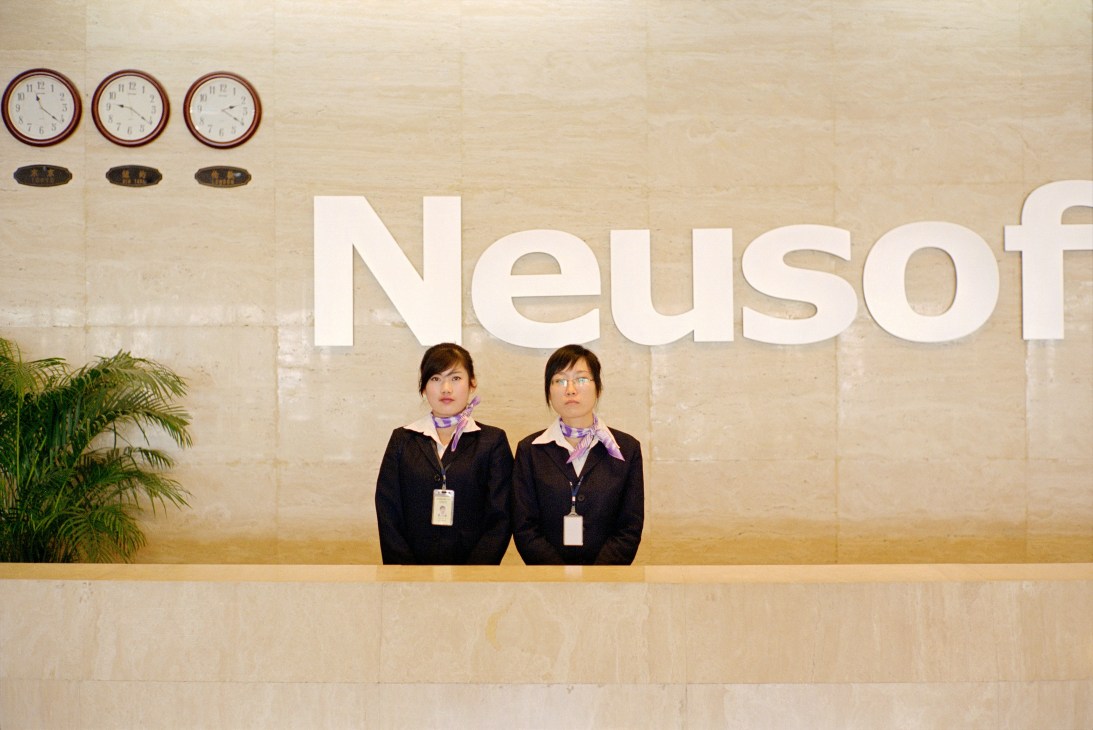 Two female receptionists stand at a Neusoft company reception desk.
