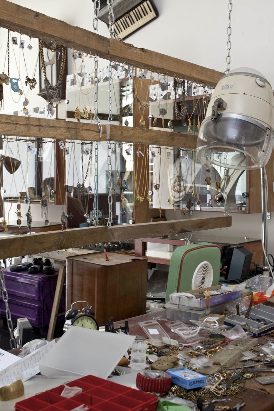 A jewellery designer's workshop with hanging necklaces and chains displayed on wooden beams above a cluttered work table.