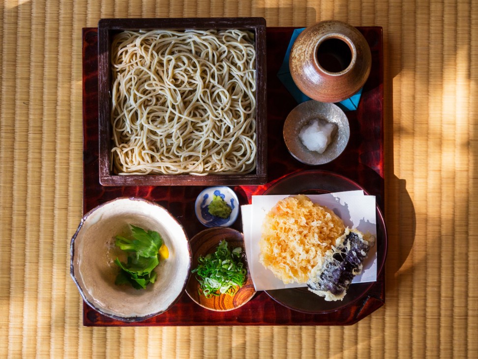 Ten seiro soba with prawn and aubergine tempura served on a dark lacquered tray with dipping sauce and condiments.