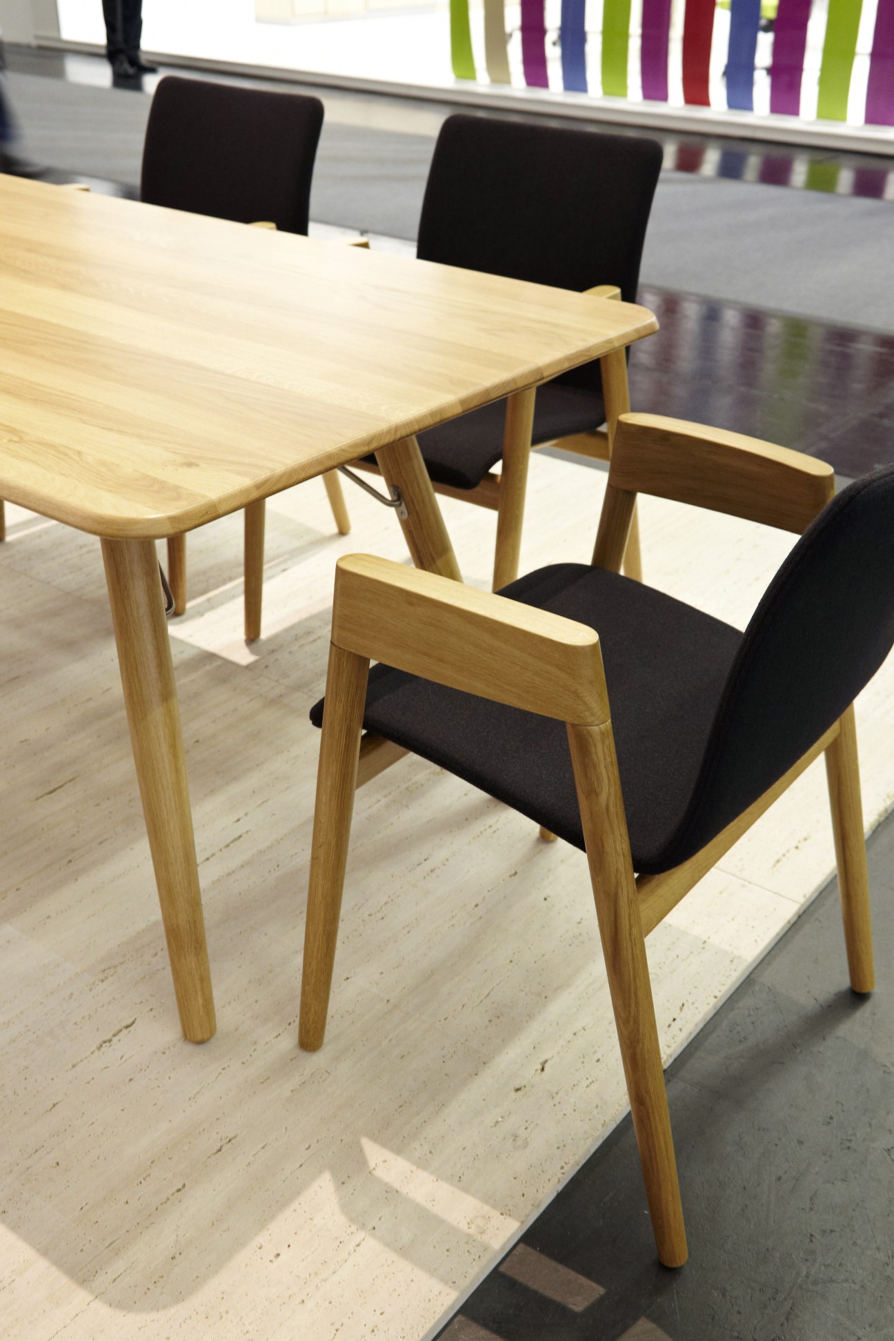 Wooden chairs with black upholstered seats at a light wood table on display at Orgatec trade fair.