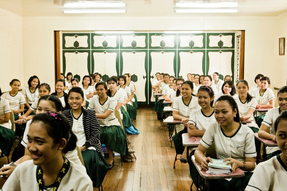 Young female students in white and dark uniforms smile during a classroom session at Punlaan School in Manila.