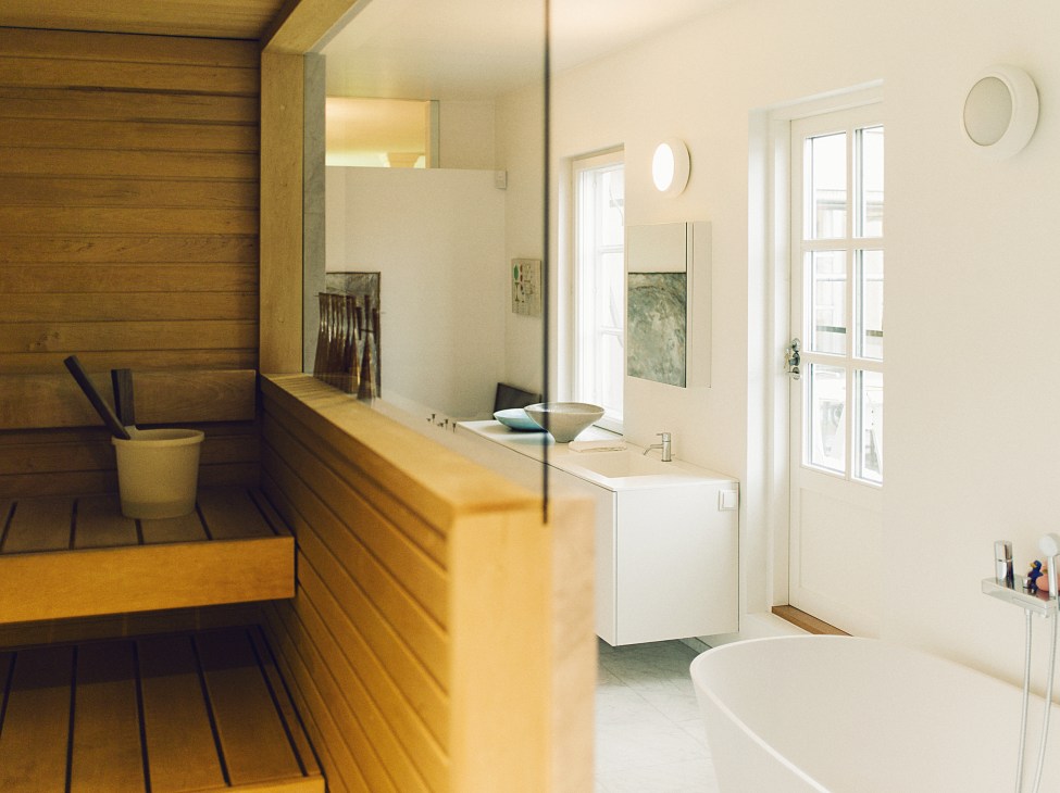 Modern bathroom with alder wood sauna, white Corian vanity, and natural light from tall windows.