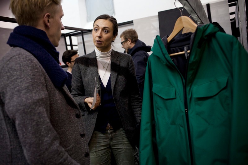 A woman in a dark blazer speaks with a man while examining a bright green jacket on display at a trade show.