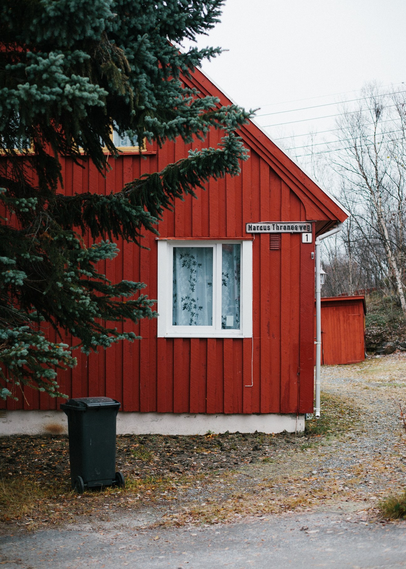 Red weatherboard house with white window frame and evergreen trees in Kirkenes, Norway.