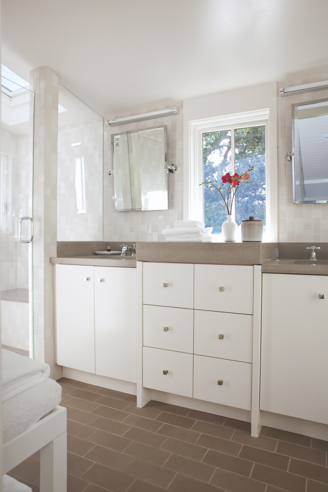 Bright bathroom with grey tile flooring, white cabinetry, grey countertop and white subway tile walls.