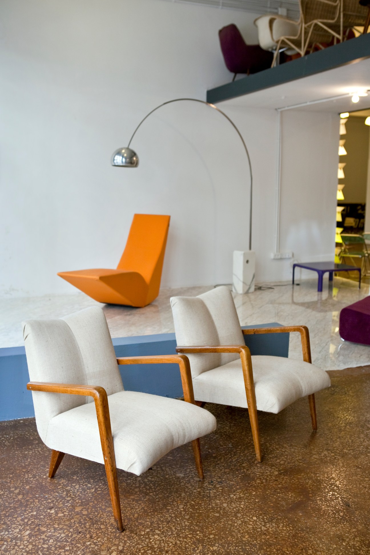 Modern furniture showroom with mid-century chairs and an arc lamp against white walls.