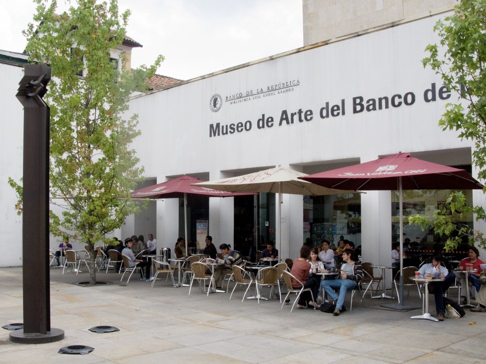 Outdoor café seating with burgundy umbrellas in front of Museo de Arte del Banco de la República in La Candelaria, Bogotá.
