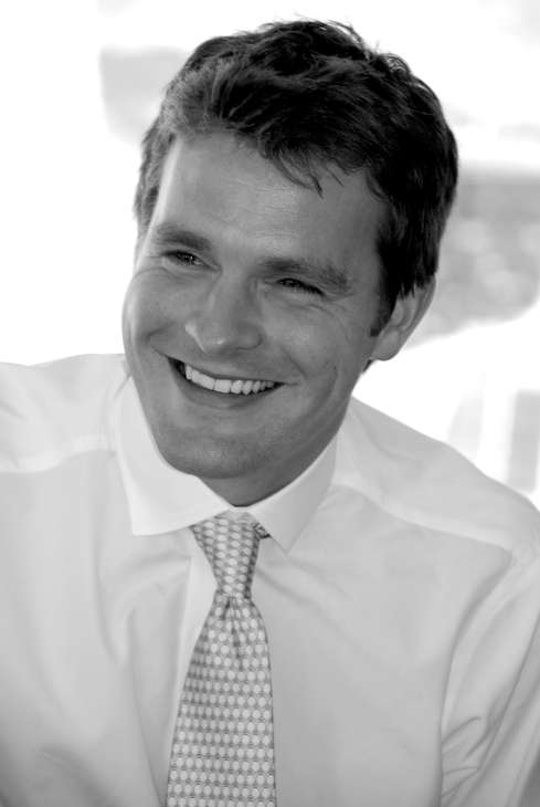 Black and white portrait of Toby Skinner, marketing director of WunderRadio, smiling at camera in white shirt and patterned tie.