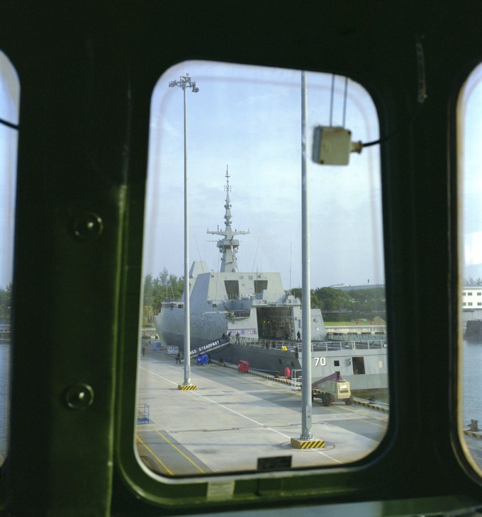 RSS Stalwart frigate docked at Changi naval base viewed through a porthole window.