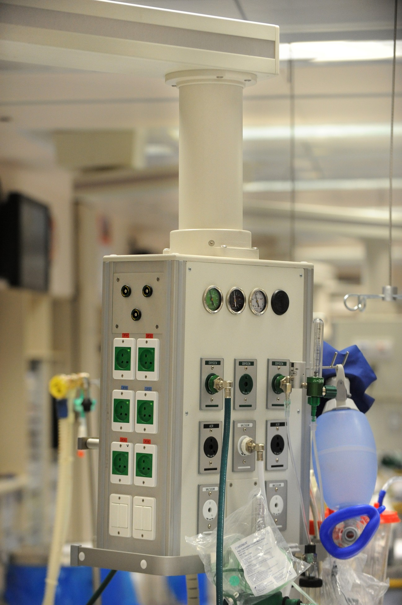 Medical equipment console mounted on a column above a hospital bed with gauges, switches and outlets.