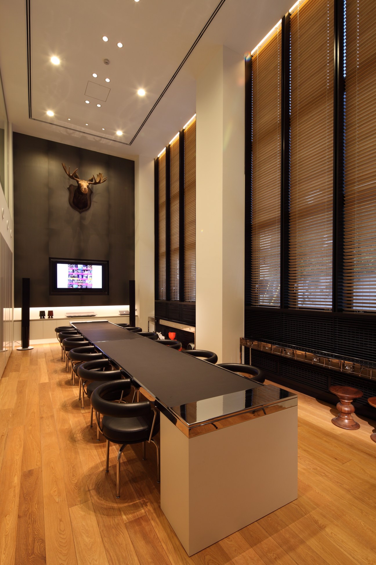 Modern meeting room with long black table, leather chairs, wood flooring, and decorative moose head on dark wall.