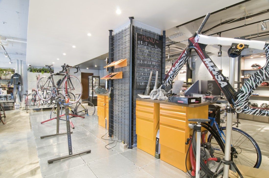 Interior of Athlonia bike shop in Tokyo showing bicycles on display stands, yellow service counter, and menu board.