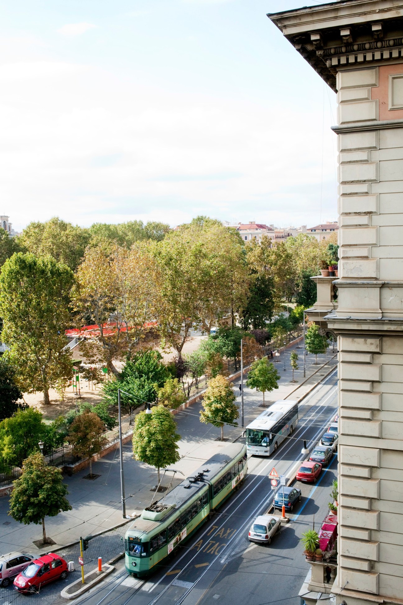 An elevated view of an Esquilino street corner with a tram, trees, and historic Roman architecture.