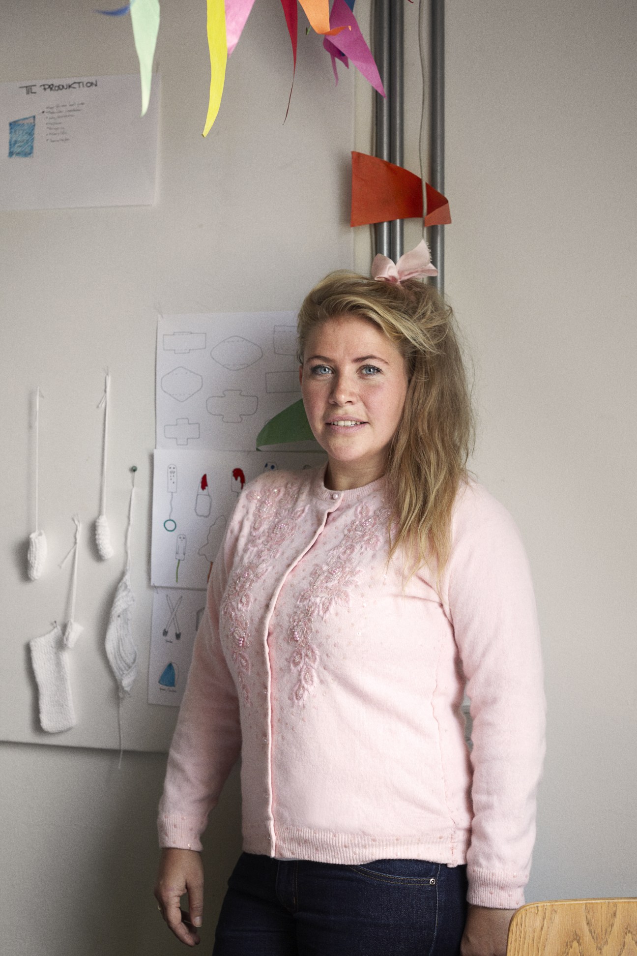Danish Design School student Sidsel Rudolph poses in front of design sketches and colorful paper models on a wall.