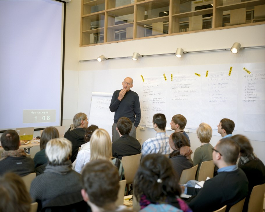 Rem Koolhaas lecturing to Strelka students in a classroom with whiteboards and yellow sticky notes.