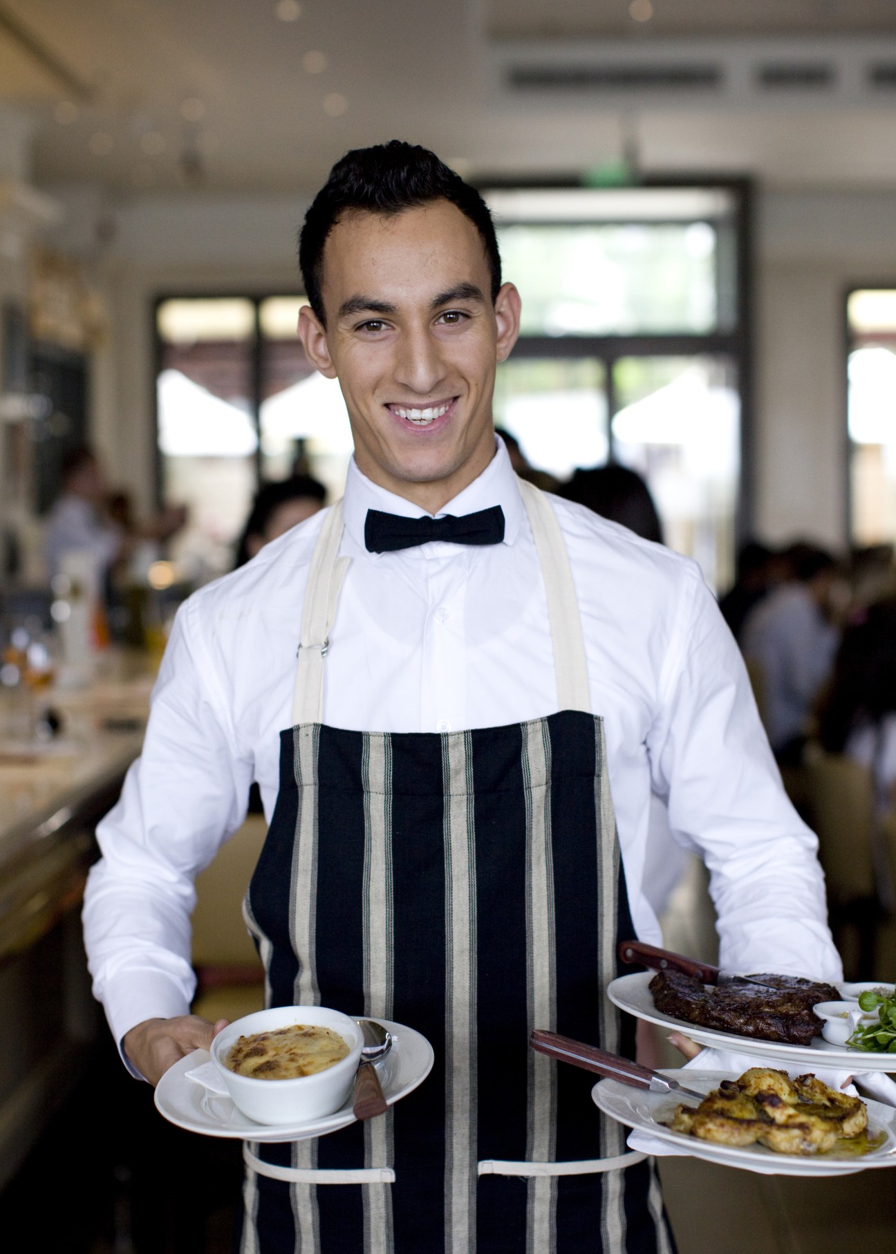 Waiter in formal attire carrying plates of food at a restaurant.