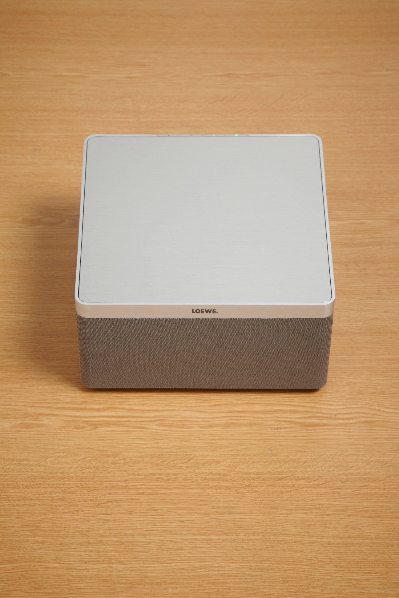 Loewe Air Speaker with white top panel and taupe fabric base on wooden surface.