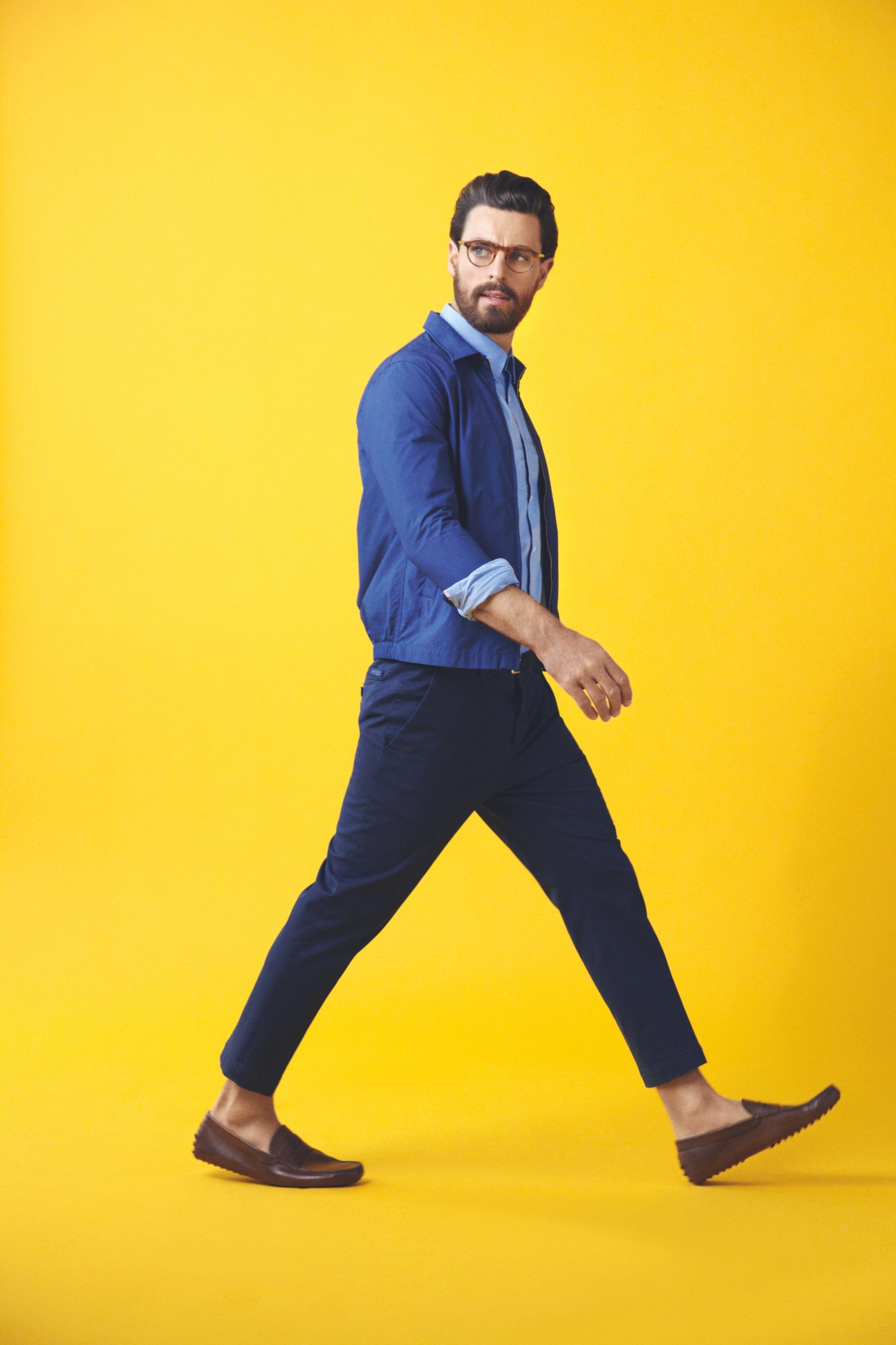 Man wearing Oliver Peoples glasses, Tomorrowland jacket, Hugo shirt, Prada trousers, Closed belt and Tod's shoes against yellow background.