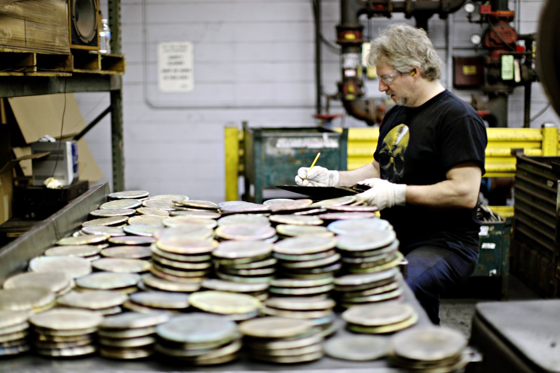 A worker in white gloves inspects stacked brass cymbals at the Zildjian factory.
