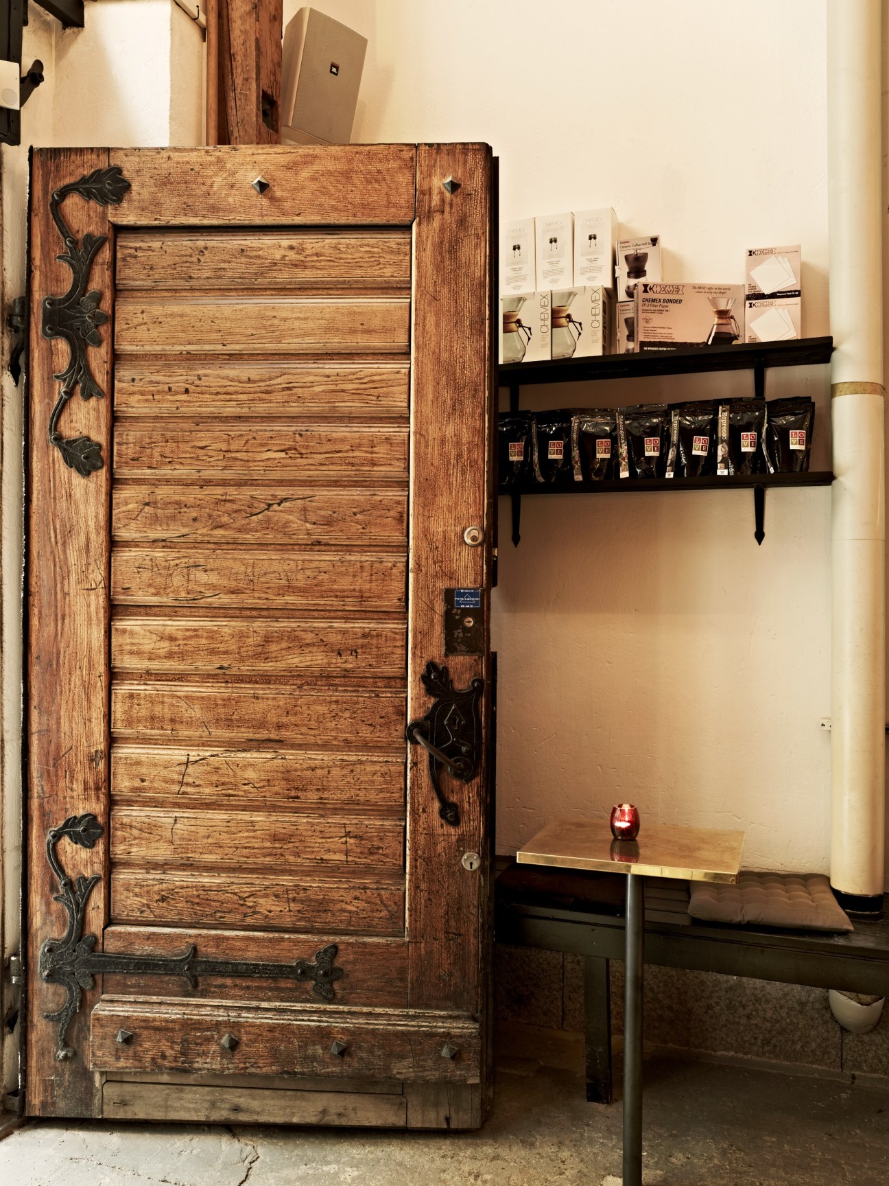 Original wooden door with ornate black metal handles at Snickarbacken 7 entrance, with black shelves displaying coffee products.