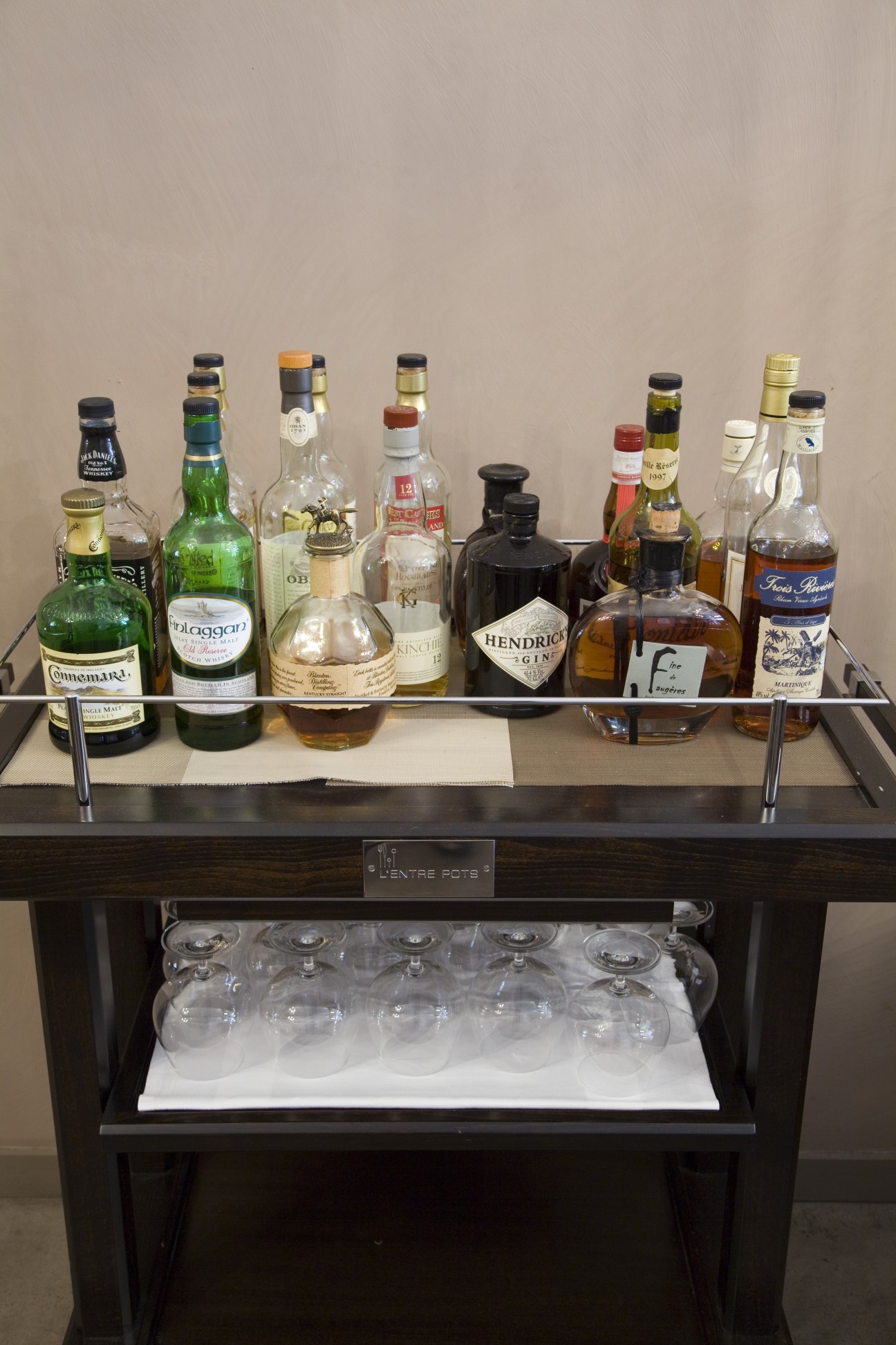 A drinks trolley at L'Entre Pots displays various spirits and liqueurs including whisky, gin, and other bottles with glasses stored below.