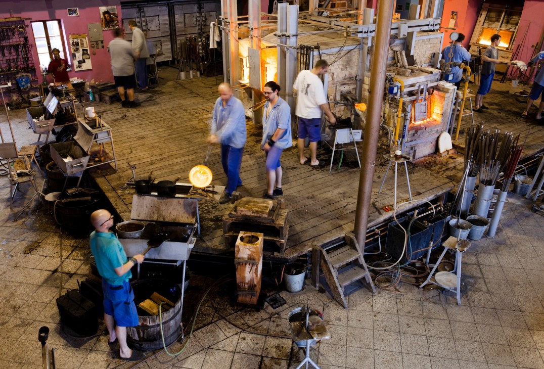 Workers in the open-air hot shop at Ajeto glassmaking factory with furnaces glowing at high temperature.
