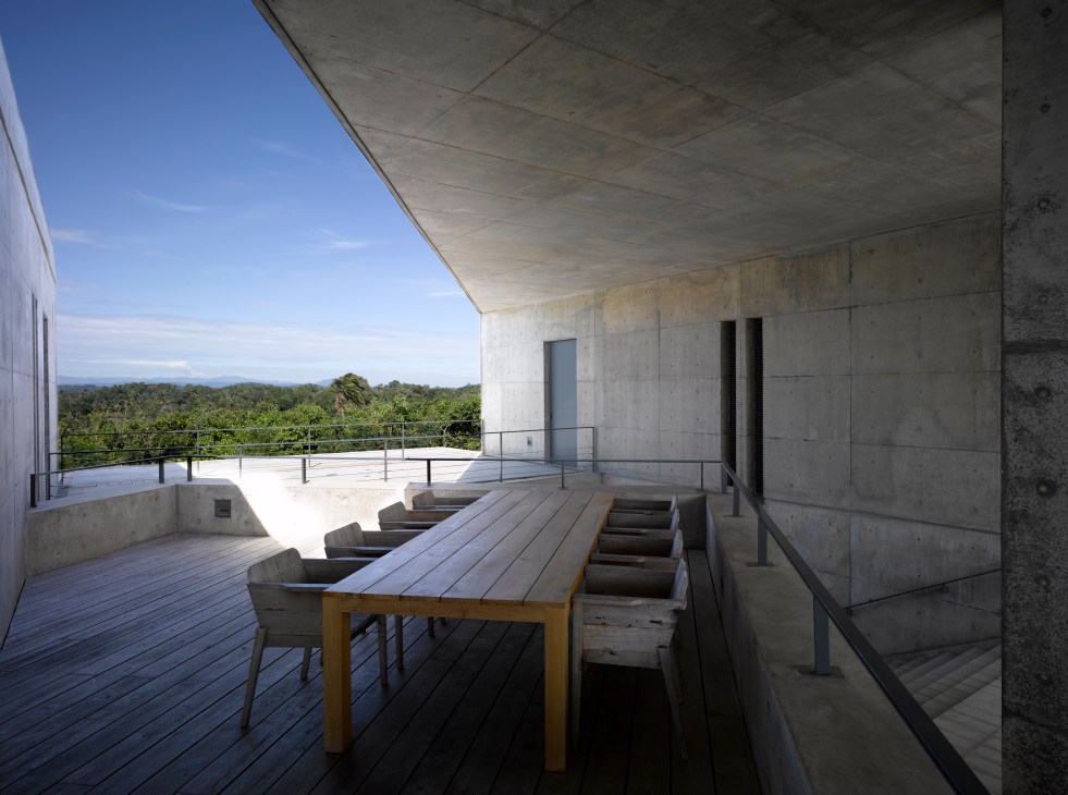 Concrete terrace with dining table overlooking lush tropical jungle and ocean vista.
