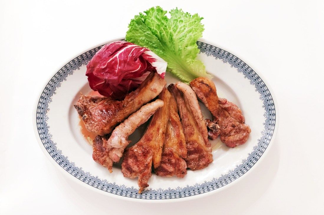 Grilled lamb chops arranged on a decorative plate with radicchio and lettuce garnish.