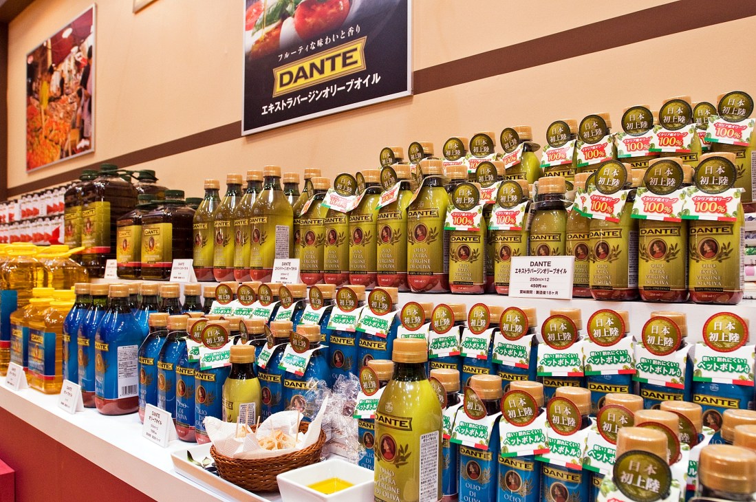 Display of Dante brand olive oil bottles and packaged products on shelves at a trade show booth.