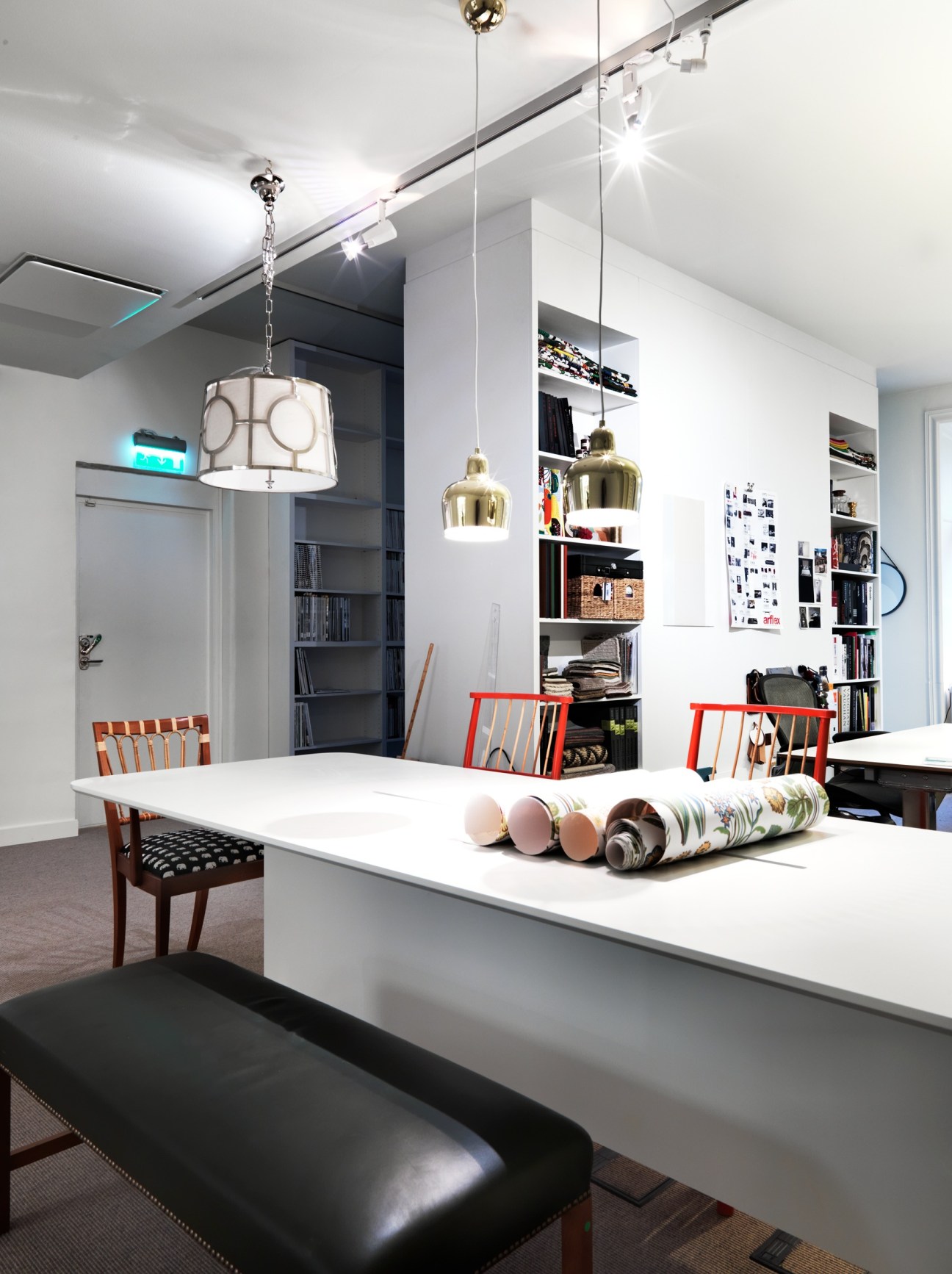 Modern kitchen with white countertops, pendant lights, open shelving, and rolled wallpaper samples displayed on the counter.