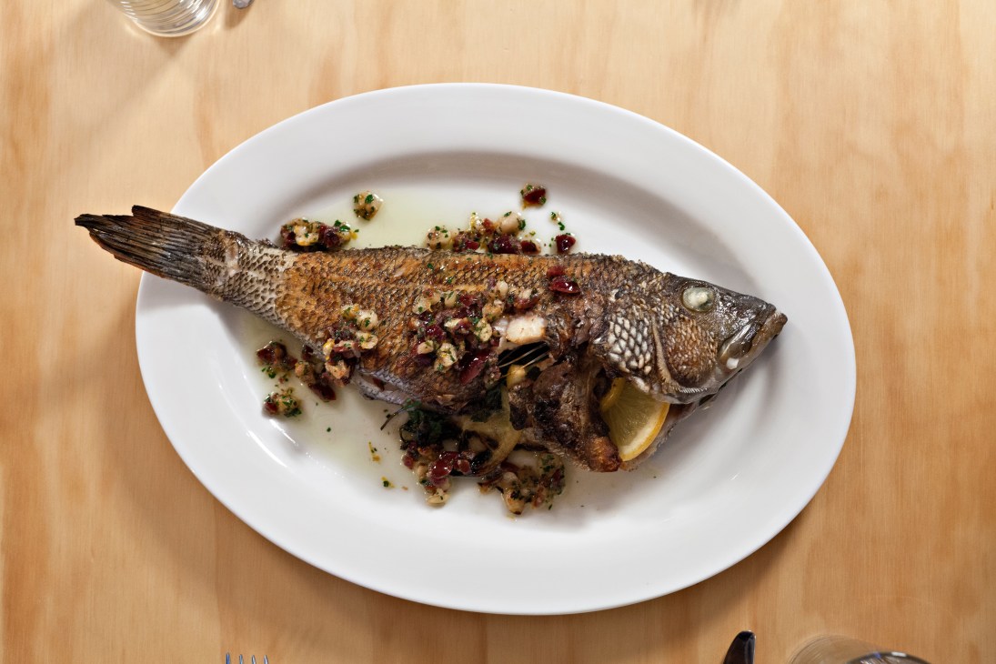 Whole roasted fish with crispy skin topped with lingonberries and garnish on a white plate.