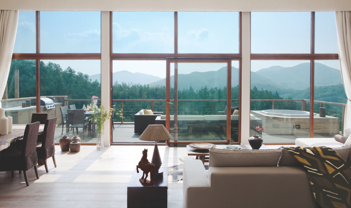Modern luxury interior with floor-to-ceiling windows overlooking forested mountains and a spa with hot tub.