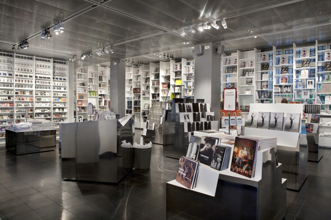 Interior of Fotografiska gallery showing white shelving units displaying photographs and books with modern track lighting.