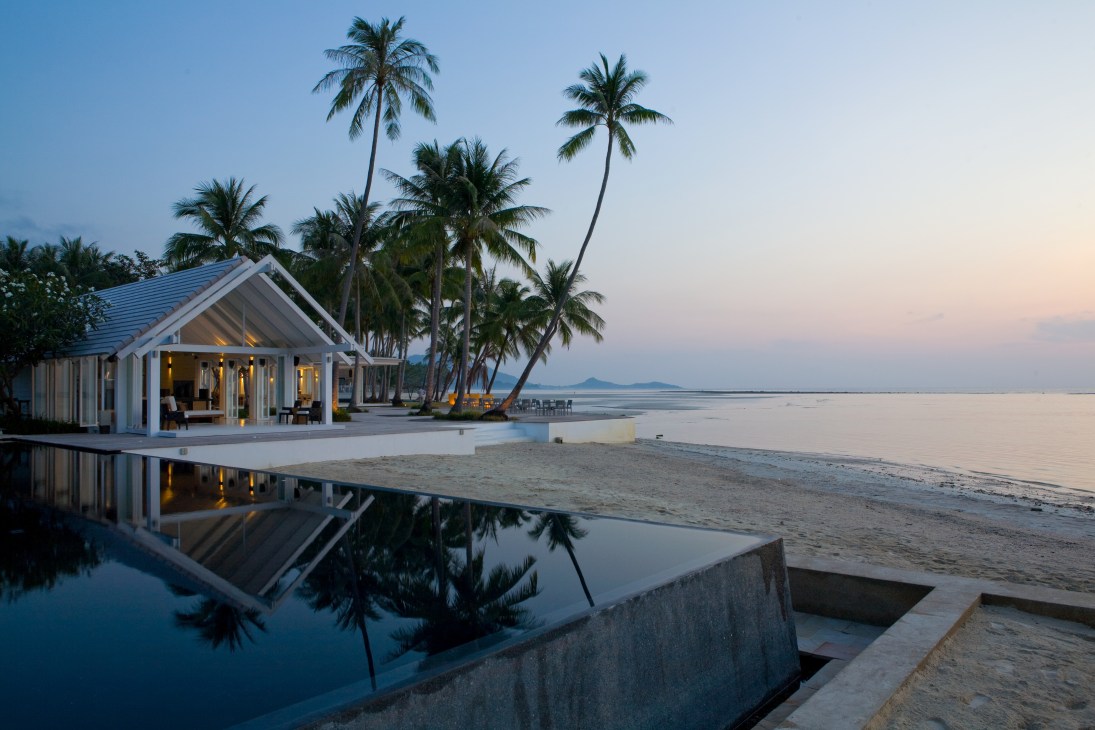 A modern beachfront villa with white walls and palm trees at dusk, reflecting in an infinity pool on Koh Samui.