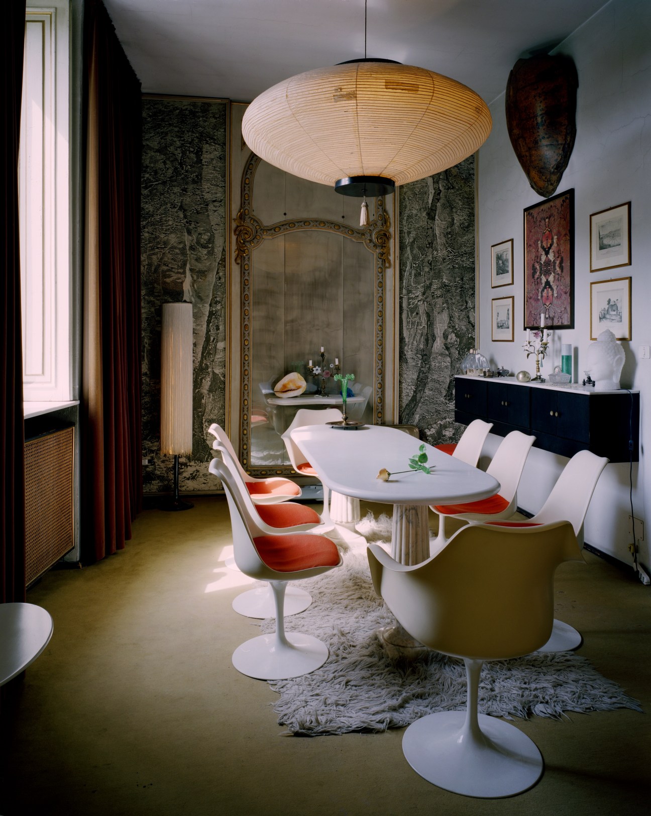 Casa Mollino dining room with modernist white table, red and white chairs, and ornate mirror.